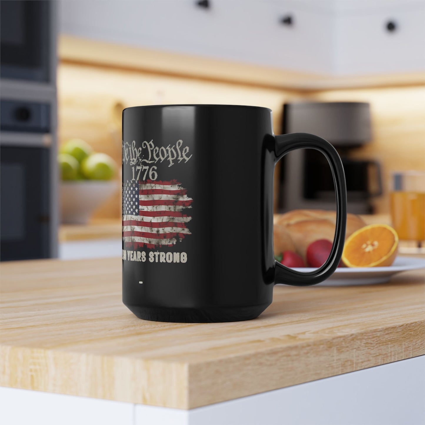 We the People 1776 black 15oz coffee mug with distressed American flag graphic on a wood kitchen counter
