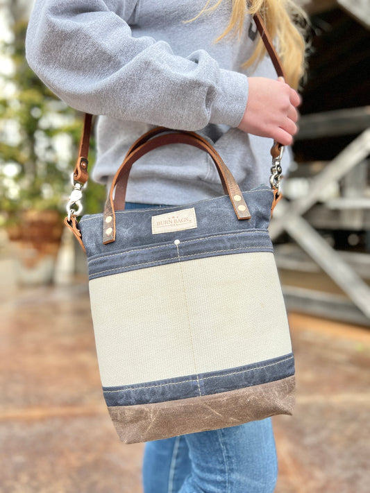 Person wearing the Charcoal Engineer Burn Bag crossbody, showing the waxed canvas body, decommissioned fire hose front panel, and leather handles while standing outdoors.