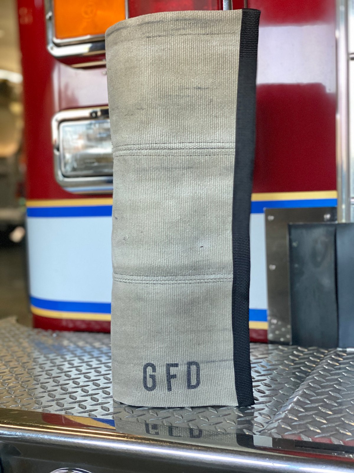 Khaki fire hose rug displayed hanging from a fire truck step, showcasing the hose texture and station markings.