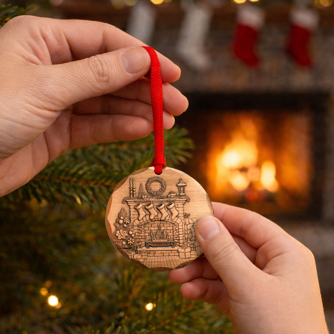 Hand holding a wooden 2026 Christmas ornament with a fireplace design in front of a lit fireplace.