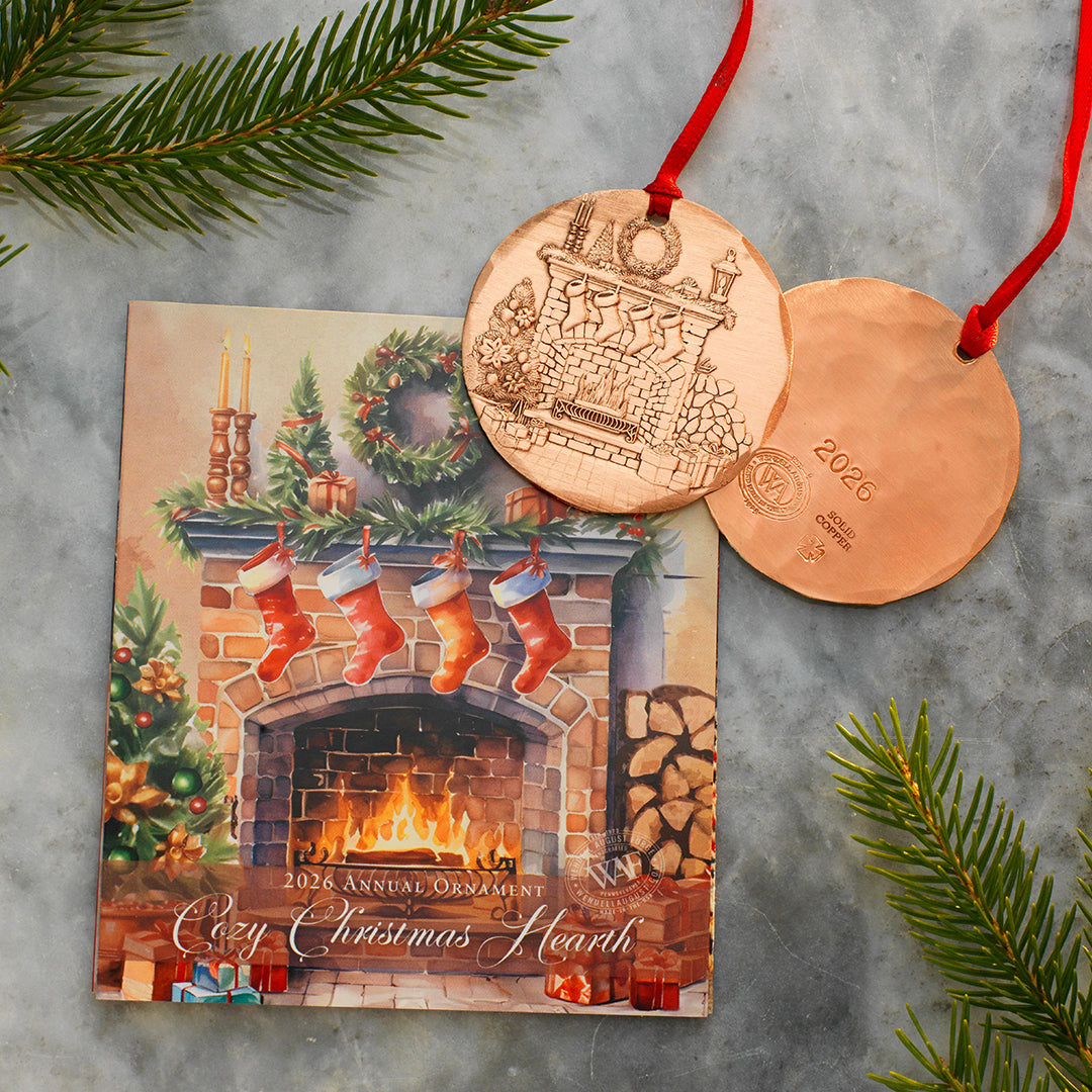 Copper Christmas ornament with a fireplace design on a card, surrounded by greenery.
