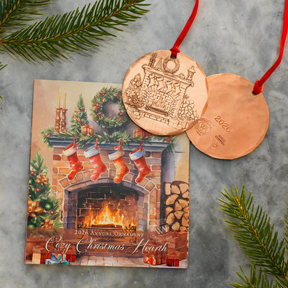 Copper Christmas ornament with a fireplace design on a card, surrounded by greenery.