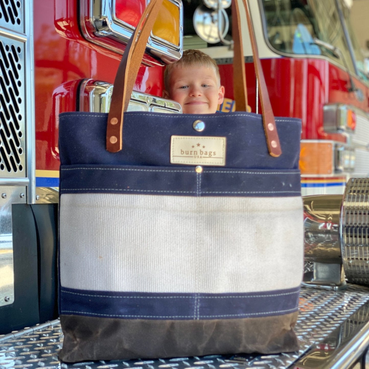 Navy Blue Classic Burn Bag made from reclaimed fire hose in front of a fire truck with a child smiling behind it.