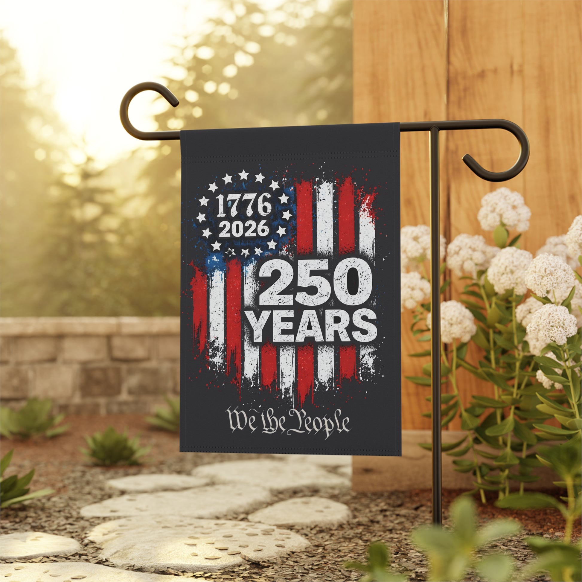 Garden flag with 1776-2026 design and  We the People text on a stand outdoors.