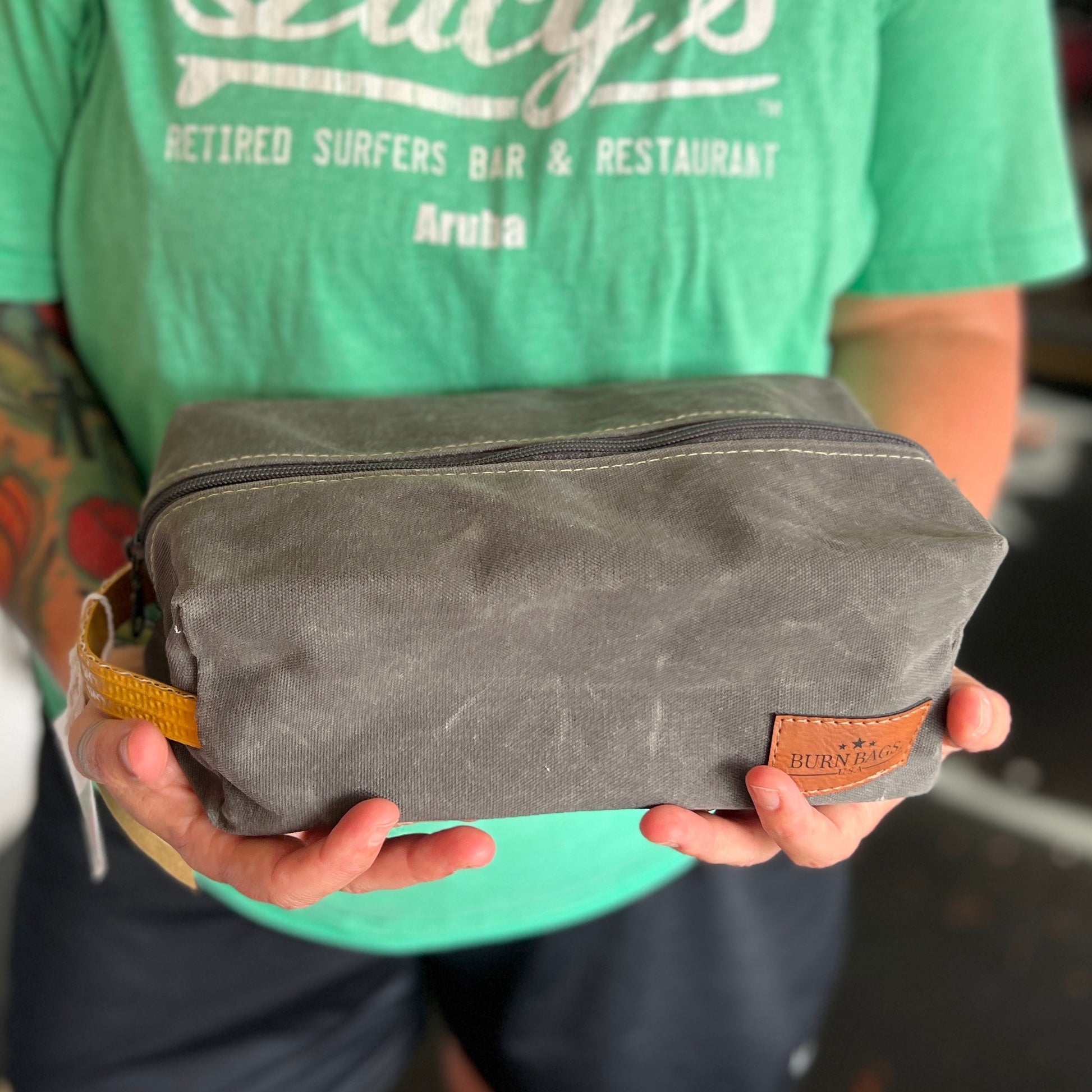 Person wearing a green shirt holding the Charcoal Gray Dopp Burn Bag in both hands, showing its size and shape