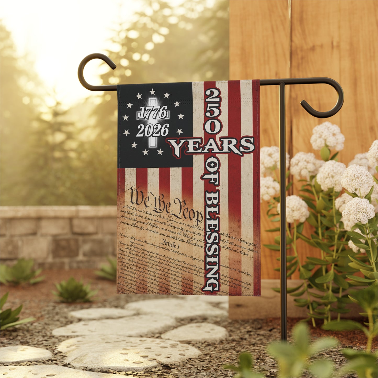 Decorative garden flag with American flag design and We the People 250 Years of Blessing text, displayed outdoors.