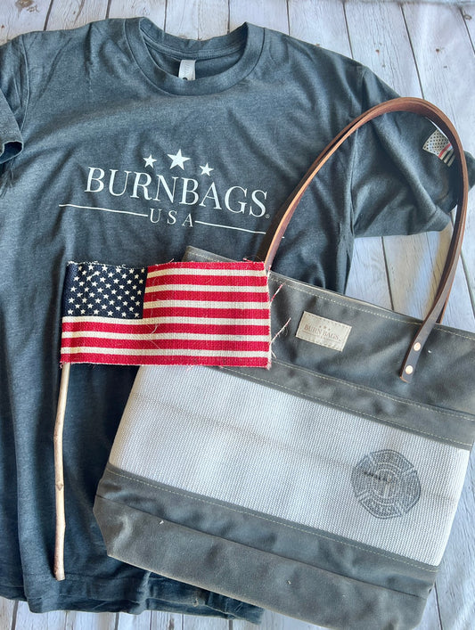 FDNY Special Edition Burn Bag with reclaimed fire hose panel displayed beside a BurnBags USA shirt and an American flag on a wooden surface.