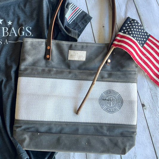 FDNY Special Edition Burn Bag made from reclaimed fire hose shown on a wooden surface with an American flag and leather straps visible.