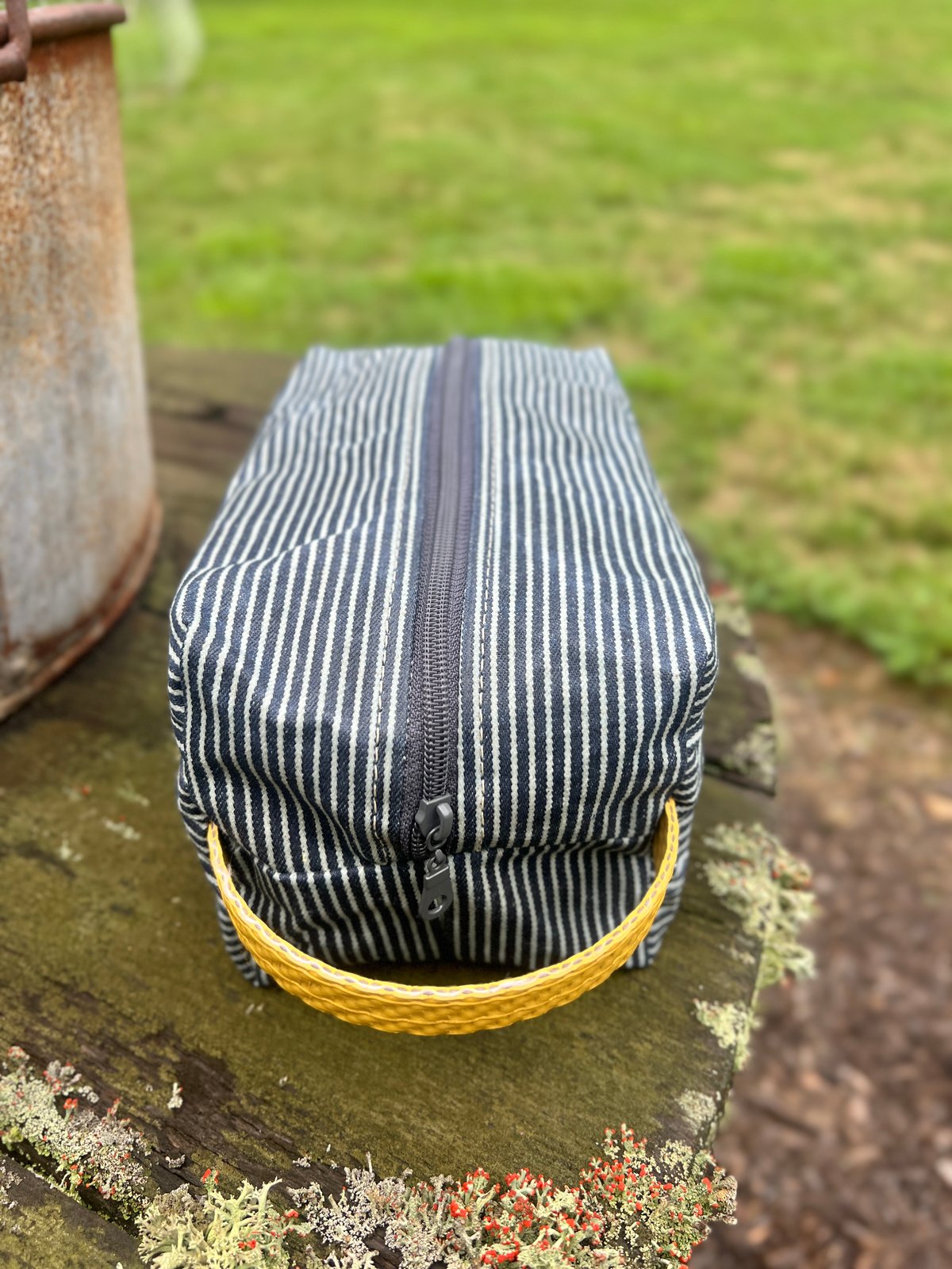 Hickory striped pouch with a yellow fire-hose handle resting on a weathered wooden surface outdoors.
