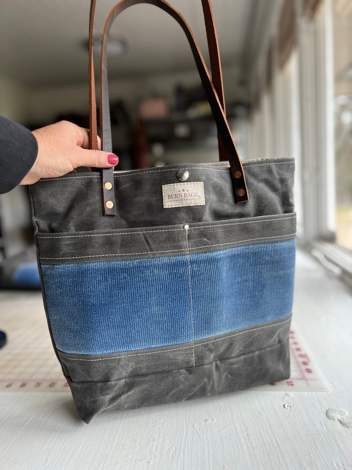 Chapel Hill Classic Burn Bag with gray waxed canvas, blue fire hose panel, and brown leather straps.