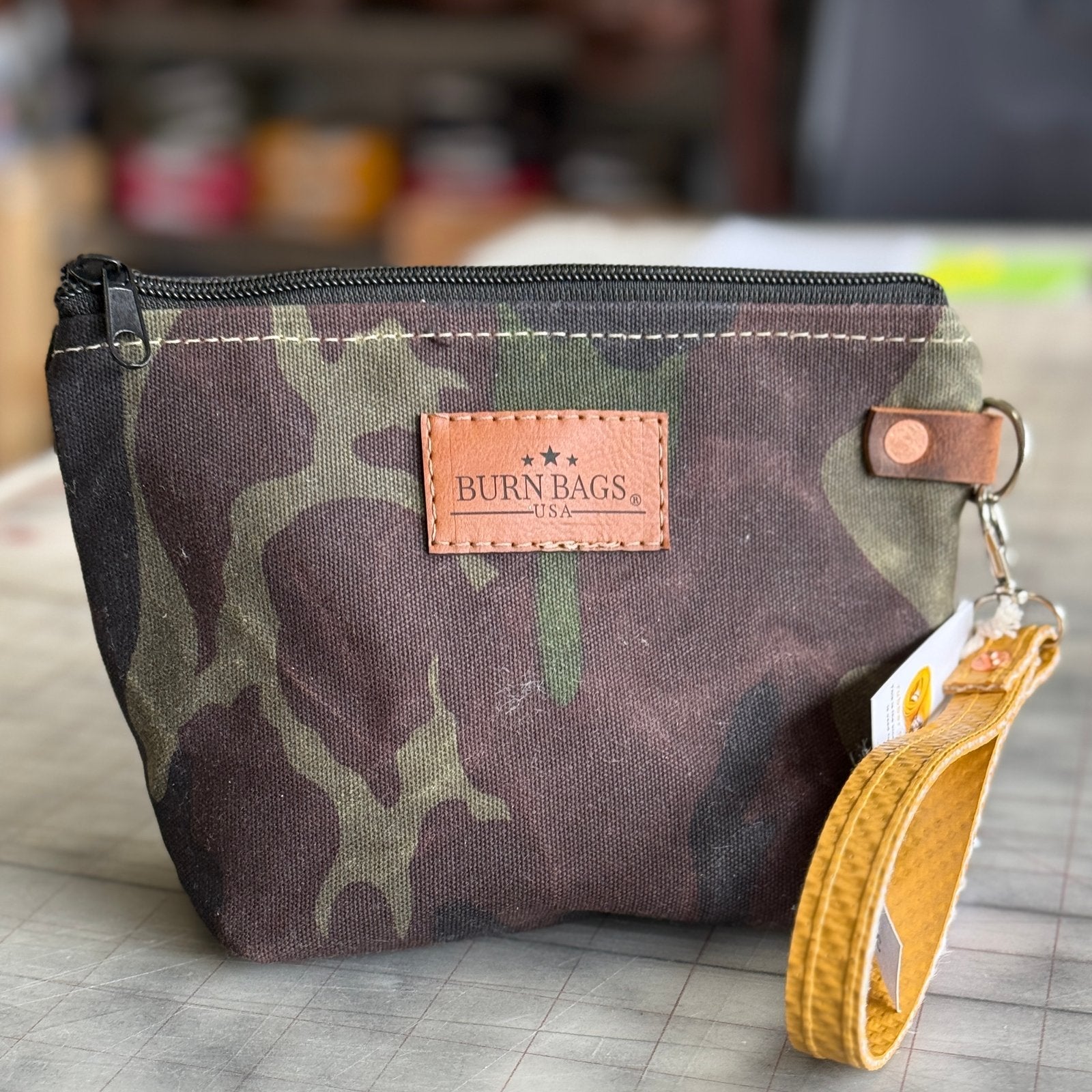 Camo clutch made from reclaimed fire hose with yellow wristlet on checkered backdrop