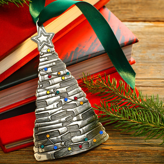 Silver Christmas tree ornament with a green ribbon on books with a wooden background