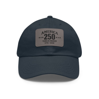 Navy blue cap with a leather patch celebrating America's 250th anniversary on a white background