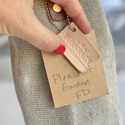 Person holding the Burn Bag Wine Carrier by its leather strap, showing the decommissioned fire hose body and attached leather tag.