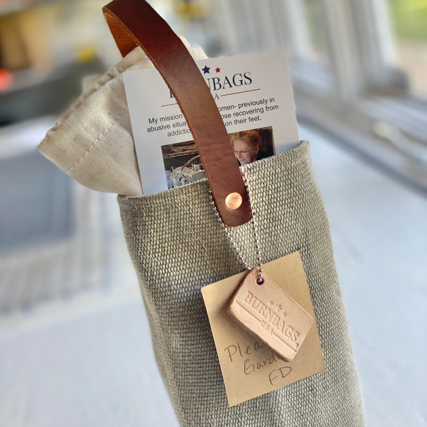 Burn Bag Wine Carrier standing upright on a table with the leather strap and square leather tag clearly visible on the front.