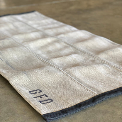 Khaki fire hose rug laid flat on a concrete surface showing textured hose panels and stamped with the department they are from on one end.