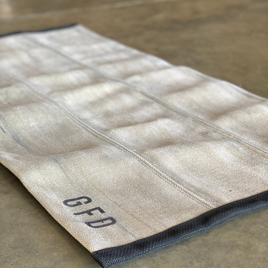 Khaki fire hose rug laid flat on a concrete surface showing textured hose panels and stamped with the department they are from on one end.