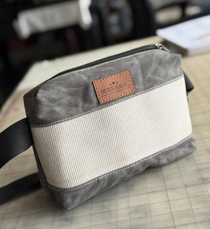 Charcoal Fanny Pack made from waxed canvas and decommissioned fire hose, shown lying flat with the adjustable strap extended behind it.