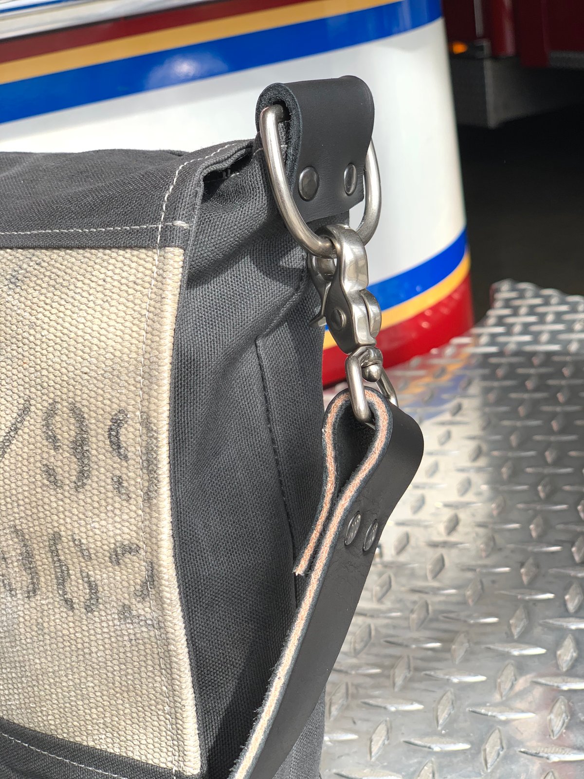 Close-up of the Charcoal Gray Messenger Burn Bag showing the side panel, leather strap attachment, and visible printed markings on the decommissioned fire hose.