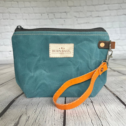 Teal waxed canvas Rubber Fire Hose Clutch with detachable orange fire-hose wristlet on wood background.